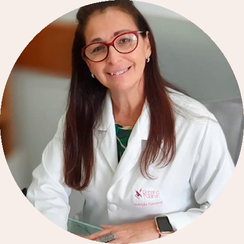 Robena Molinari sentada à mesa do consultório, de jaleco branco e sorrindo